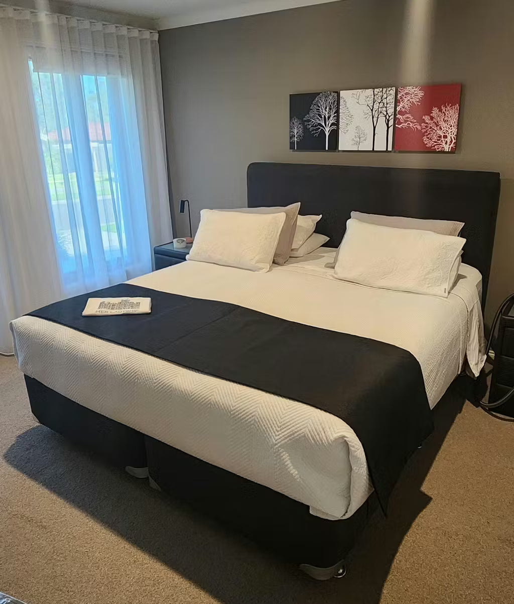 Bedroom with a neatly made bed. Bedezy is installed under this mattress on the ensemble suite, showing that detailed corners can be done using Bedezy with decorative pillows and wall art.